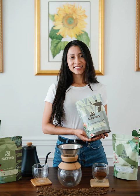 Nativa's owner holding a package of Nativia coffee in a home setting with coffee-making equipment and coffee beans.